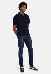 Polo shirt à manches courtes bleu marine avec un col plat, associé à un jean slim bleu foncé et des baskets bleu marine avec des rayures blanches.