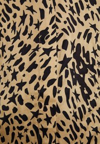 Tessuto beige con forme astratte nere e motivi a stelle, con dettagli di cucitura visibili, che trasmette un design texturizzato.