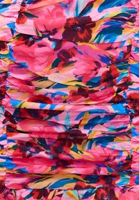 Tissu rose vif avec des fleurs rouges et bordeaux foncé, des feuilles bleues et jaunes, et des détails de couture froncée.