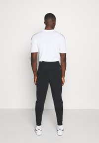 Vit t-shirt med kort ärm och svarta joggingsbyxor. T-shirten har rund halsringning; joggingsbyxorna har elastiska muddar och sidofickor. Vita sneakers.