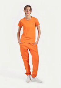 Orange træningstøjssæt bestående af en kortærmet t-shirt og joggingbukser. Bomuldsblandet stof med elastiske manchetter og et lille logodetalje.