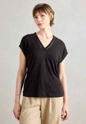 Top nero a maniche corte con scollo a V, caratterizzato da un dettaglio testurizzato sul collo, realizzato in materiale morbido, abbinato a pantaloni a vita alta di colore chiaro.