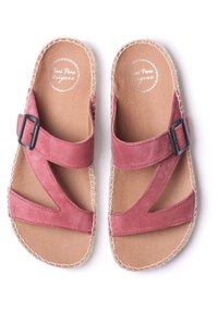 Pink suede sandals with two crossed straps, featuring a black metal buckle, and a tan cushioned insole with stitched edging.