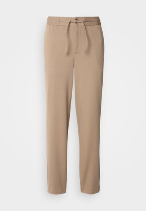 Beiga mjukisbyxor gjorda av mjuk bomull, med elastisk midja, dragsko, slim fit och raka ben utan mönster.