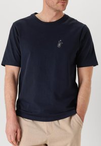 T-shirt di cotone blu navy con maniche corte, scollo rotondo e una piccola grafica sul petto. Tessuto liscio e vestibilità rilassata.