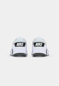 Nike-sko med en hvid overdel, sorte accenter og et fremtrædende logo på hælen, der har et lavprofileret design og en tekstureret sål.