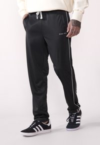 Black athletic pants with white side stripes, drawstring waist, and logo "PIER ONE" on the front. Smooth fabric with a relaxed fit.