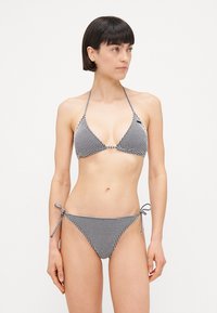 Melnā un baltā ginekāra bikini ar trīsstūrveida topu un regulējamiem saišu apakšiem. Materiāls ir viegls un gluds.