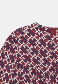 Rotes Kleid mit einem geometrischen Muster in Weiß und Blau. Hat einen gerundeten Ausschnitt und gerafftes Material für Textur.