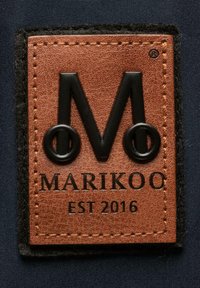 Patch en cuir marron avec un "M" noir en relief et des accents circulaires, dotée des détails textuels "MARIKOO" et "EST 2016", bordée de tissu noir.