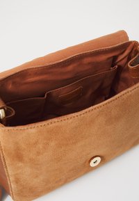 Brun ruskinds håndtaske med en glat overflade, der har en guldbutton-lukning og indvendige lommer i et matchende brunt stof.