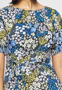 Kwiatowa sukienka w czarnym kolorze z żywymi niebieskimi, różowymi i żółtymi kwiatami; krótkie bufiaste rękawy; dopasowana góra z ozdobnym wiązaniem w talii.
