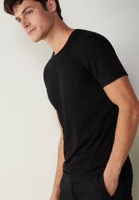 Schwarzes T-Shirt mit kurzen Ärmeln im figurnahen Schnitt, aus weichem Stoff mit glatter Textur. Mit klassischem Rundhalsausschnitt.