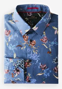 Chemise bleue à manches longues boutonnée avec motif floral multicolore et design géométrique contrasté à l’intérieur des poignets, soigneusement pliée avec le col visible.