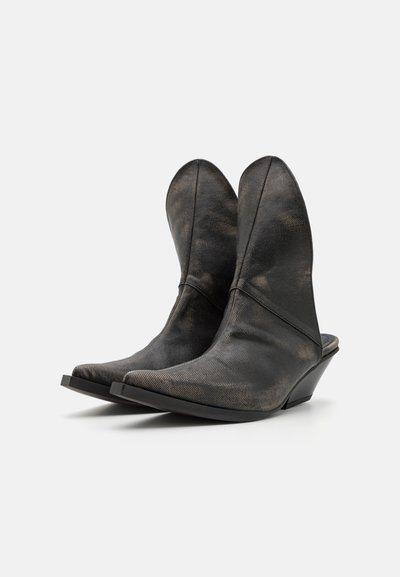 Bottes noires en cuir jusqu'à la cheville avec un bout pointu, un talon compensé haut et des revers évasés distincts. Surface texturée avec un léger éclat.