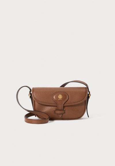 Sac en cuir marron à bandoulière avec un rabat incurvé, des embellissements en or, et un logo décoratif. La sangle est ajustable et présente une texture lisse.