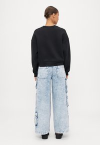 Μαύρος κοντός φούτερ με oversized εφαρμογή, συνδυασμένος με ανοιχτόχρωμα φαρδιά cargo τζιν παντελόνια που διαθέτουν πλευρικές τσέπες και φθαρμένες λεπτομέρειες.