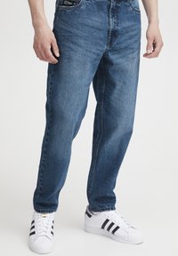 Blå denimjeans med avslappet passform, rett ben, fem lommer og minimalistiske detaljer; brukt med hvite joggesko.