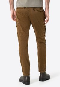 Brown cargo pants with a slim fit, made of soft cotton. Features side pockets and a back pocket. Flat front, tapered ankle, and subtle stitching.