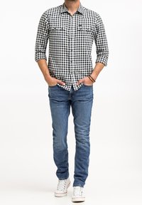 Czarna i biała koszula w kratę z długim rękawem, z przednimi kieszeniami, w zestawieniu z niebieskimi dżinsami slim fit i białymi trampkami.