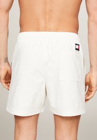 Costumi da bagno bianchi da uomo con cintura elastica, tasca posteriore e patch con logo. Realizzati in tessuto leggero con orlo piatto.