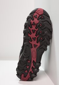 Schwarze Wanderschuhsohle mit tiefen, aggressiven profilierten Mustern und roten Akzenten. Texturiertes Gummi verbessert den Grip und die Haltbarkeit.