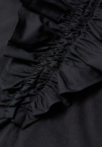 Haut en tissu noir avec un détail central à volants à texture froncée. Le tissu lisse environnant complète l'accent texturé.