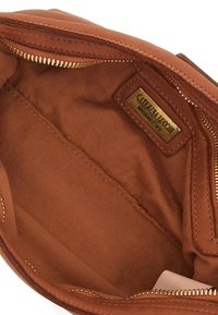Interno della borsa in pelle marrone con fodera in tessuto beige, zip dorata e etichetta con logo. Texture liscia e dettagli di cucitura minimi.