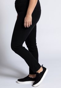 Černé džíny z denimu se slim fit střih, obsahující kapsy a hladký povrch. Noseny s černými semišovými nazouvacími botami s bílou podešví.