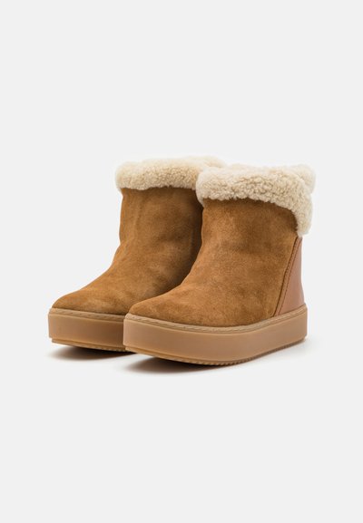 Brown suede ankle boots with a cream faux fur cuff and a thick beige rubber sole, featuring stitched detailing on the upper.