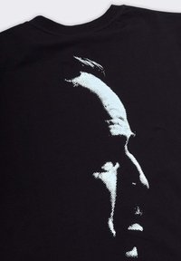 T-shirt nera con una grafica stilizzata e pixelata di profilo laterale in azzurro. Il tessuto appare morbido con un collo a giro standard.