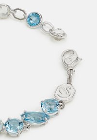 Pulsera de plata que presenta piedras azules y transparentes de diversas formas, con un cierre de langosta y un encantador hexagonal con un diseño de cisne.