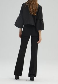 Svart kortärmad blus med trumpetärmar, kombinerad med svarta smala byxor. Materialet verkar vara slätt; den övergripande designen är stilren och modern.