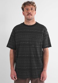 T-shirt nera con motivo, dotata di collo a giro e maniche corte, con dettagli a taschino sul lato sinistro del petto e disegni geometrici testurizzati.