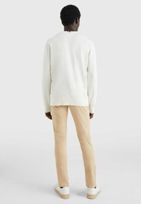 Maglione bianco a maglia con dettagli a coste, abbinato a pantaloni beige chiaro. Presenta un piccolo accento rosso e blu sul collo.