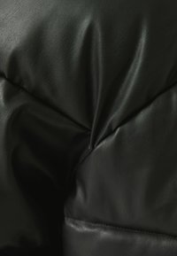 Černý kožený polštář s vrásčitou texturou a měkkým vzhledem. Obsahuje prošité švy a výrazné záhyby pro zvýšení dimenze.