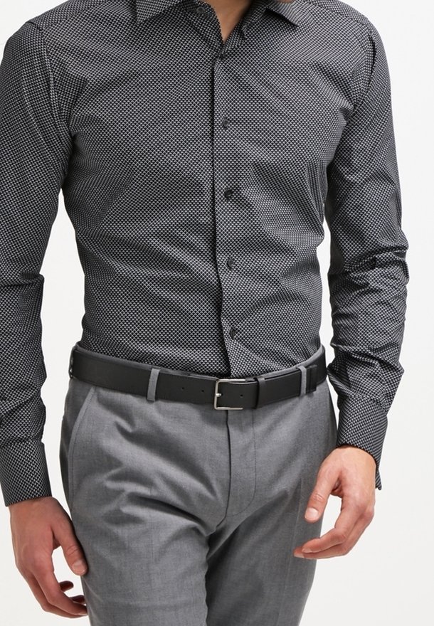 Homme portant une chemise ajustée à boutons à motif noir et blanc rentrée dans un pantalon de costume gris avec une ceinture noire.