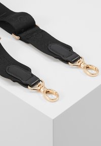 Tracolla regolabile nera con accessori in metallo dorato e dettagli in pelle, con una superficie in tessuto testurizzato. Ideale per borse o accessori.