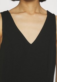 Czarna sukienka bez rękawów z dekoltem w kształcie litery V, gładką fakturą i tonalnym przeszyciem, podkreślająca dopasowaną sylwetkę i czyste linie.