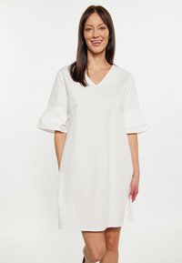 Weißes Kleid mit V-Ausschnitt, ausgeweiteten kurzen Ärmeln und glatter Textur, das eine lockere Passform und seitliche Taschen bietet.