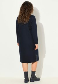 Laivastonsininen pitkähiha dressi suoran siluetin ja ribattujen hihansuiden kanssa, jossa on sivujatkoketju. Yhdistetty mustiin nauhakorkokenkiin.