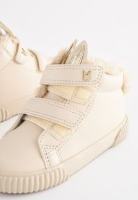 Beige high-top shoes made of smooth leather with faux fur lining, two Velcro straps, and decorative bunny ear accents.