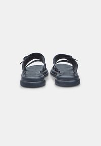 Juodos minimalistinio dizaino šlepetės, turinčios dvi plačias dirželius ir tekstūruotą pado apdailą. Guminis padas užtikrina stabilumą ir paramą.
