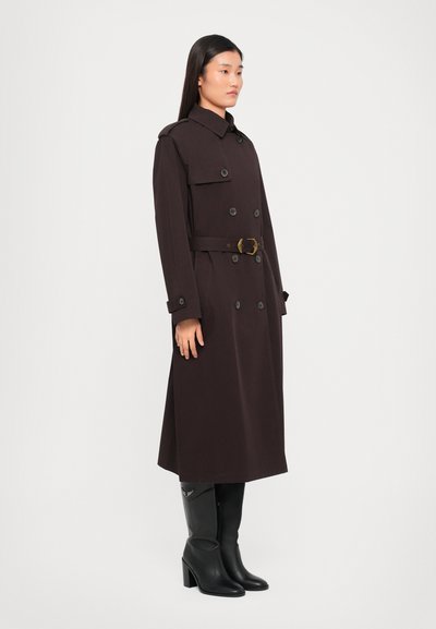 Trench coat lung maro, dintr-un material texturat, cu un front cu două rânduri de nasturi, talie cu centură și epoleți proeminenți la umeri. Botine negre cu toc.