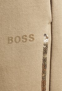 Beige Strickpullover mit "BOSS" in passender Farbe gestickt; verfügt über eine vertikale Linie aus Pailletten auf einer Seite für zusätzlichen Detail.