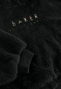 Felpa nera in pile con logo ricamato dorato "BAKER by Ted Baker". Polsini a costine e tessuto morbido e testurizzato.