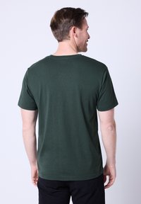 Ciemnozielona koszulka z krótkim rękawem wykonana z miękkiego materiału, z okrągłym dekoltem i prostą, gładką fakturą. Bez widocznych logo ani wzorów.