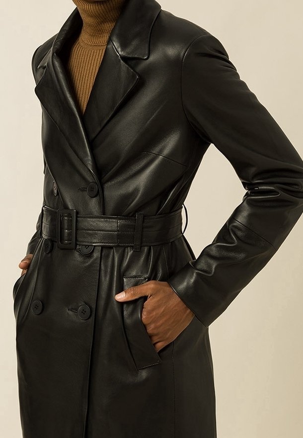 Černý kožený trench kabát s klopovými límečky, dvouřadým zapínáním a páskem v pase. Obsahuje boční kapsy a hladkou texturu.