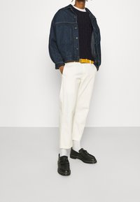 Jeansjacka, marinblå stickad tröja, gul bälte, vita byxor, svarta skor med fransdetalj och ljusgrå strumpor.