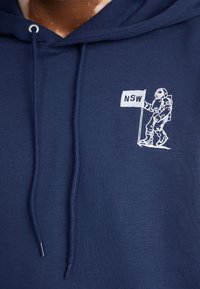 Hoodie bleu marine en tissu doux, avec un graphique d'astronaute blanc et le texte "NSW" sur le devant. Capuche avec cordons de serrage.